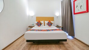 A neatly made bed with a geometric-patterned blanket and two decorative pillows, a bedside table with a phone, and a framed picture on the wall. - Fabhotel Destiny Inn (Gurugram)