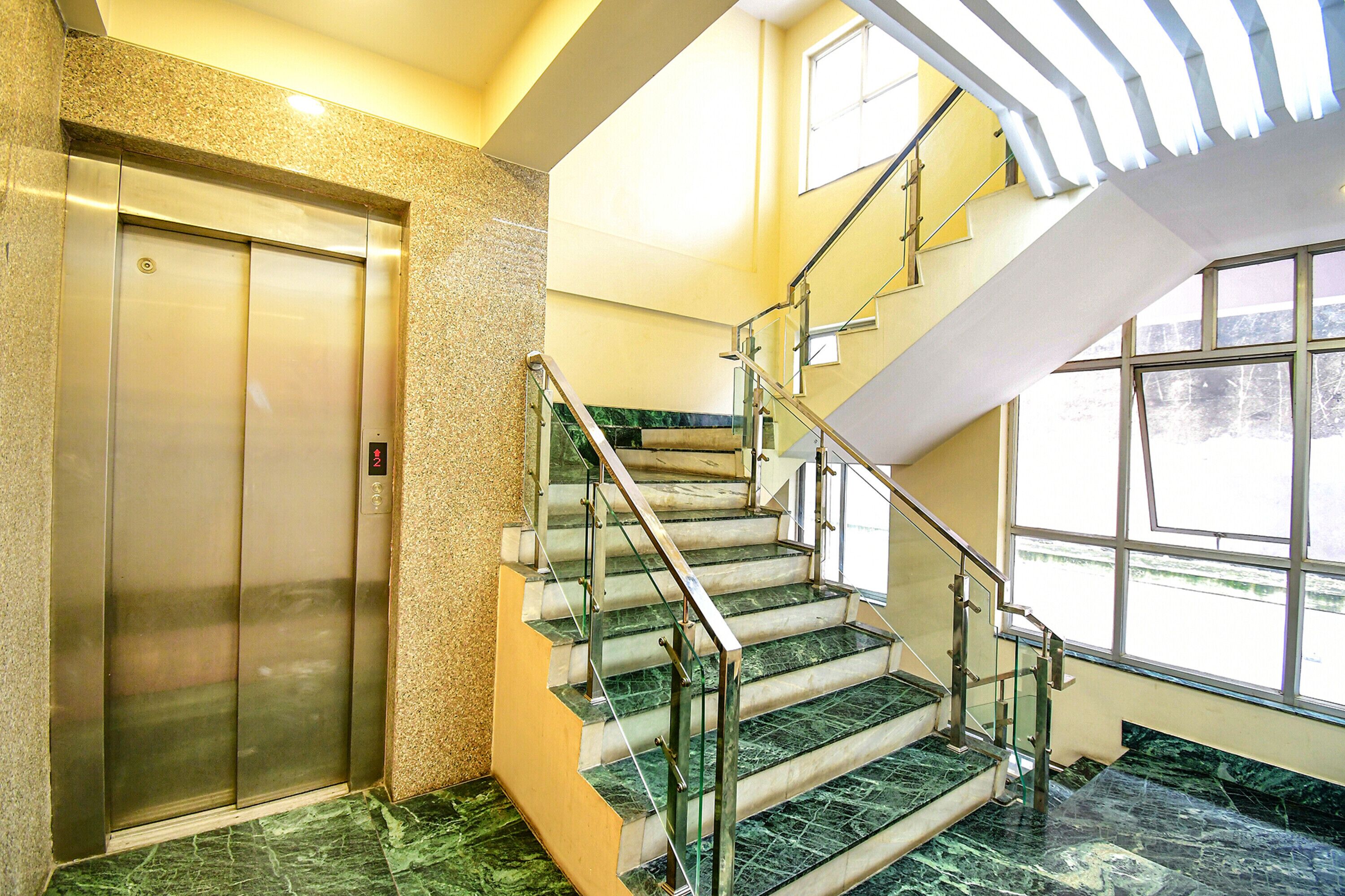An interior with a marble staircase, a glass railing, and a modern elevator.