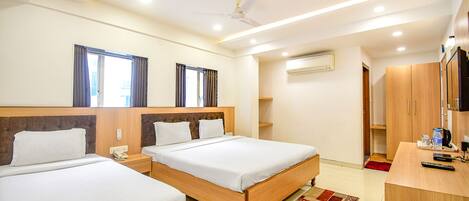 A hotel room with two beds, a desk, a chair, a ceiling fan, and an air conditioning unit.