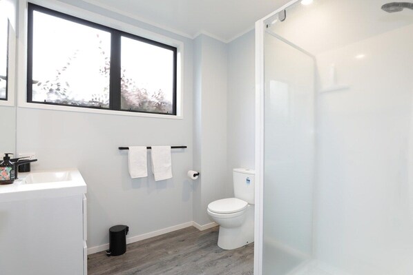 A bathroom with a white sink, toilet, and shower. There is a window above the sink and a towel rack on the wall.