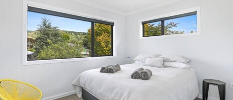 A bedroom with a bed, two windows, a chair, and a small stool.