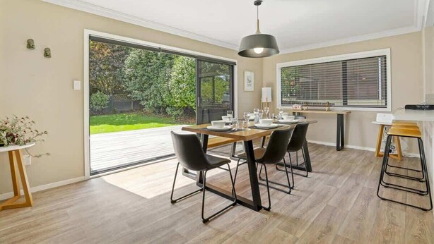 Uma área de jantar moderna com uma mesa grande, cadeiras pretas e uma luminária pendente.