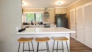 Cozinha moderna com ilha central, banquetas, forno embutido e geladeira.