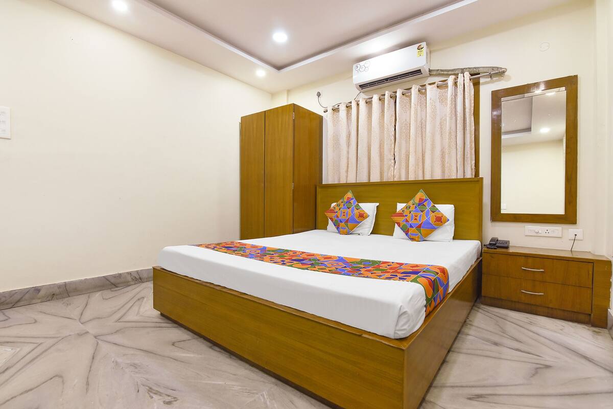 A hotel room with a bed, a wooden wardrobe, a bedside table with a phone, and a mirror on the wall.