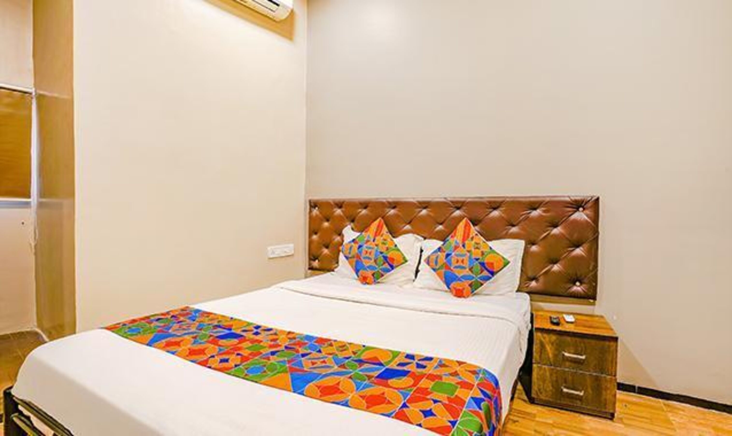 A hotel room with a bed, a nightstand, and a wooden floor.
