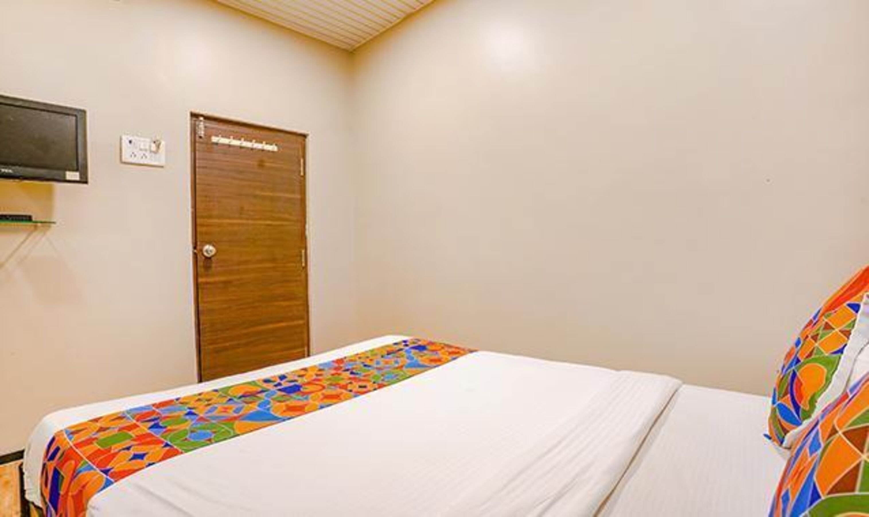 Un dormitorio con una cama, una puerta de madera y un televisor montado en la pared.
