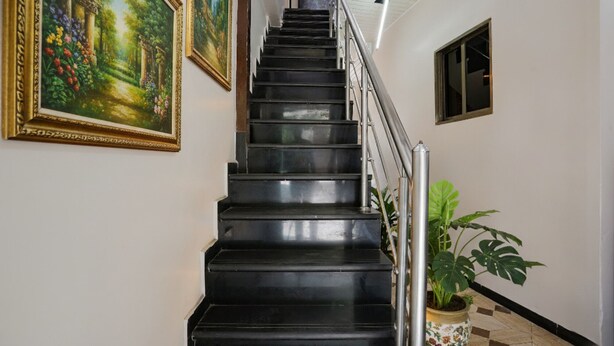 A black staircase with metal railings, flanked by two framed paintings and a potted plant. - FabHotel Comfort stay (Mumbai)