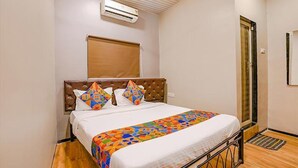 A bedroom with a bed, a window with blinds, an air conditioning unit, and a door. - FabHotel Comfort stay (Mumbai)