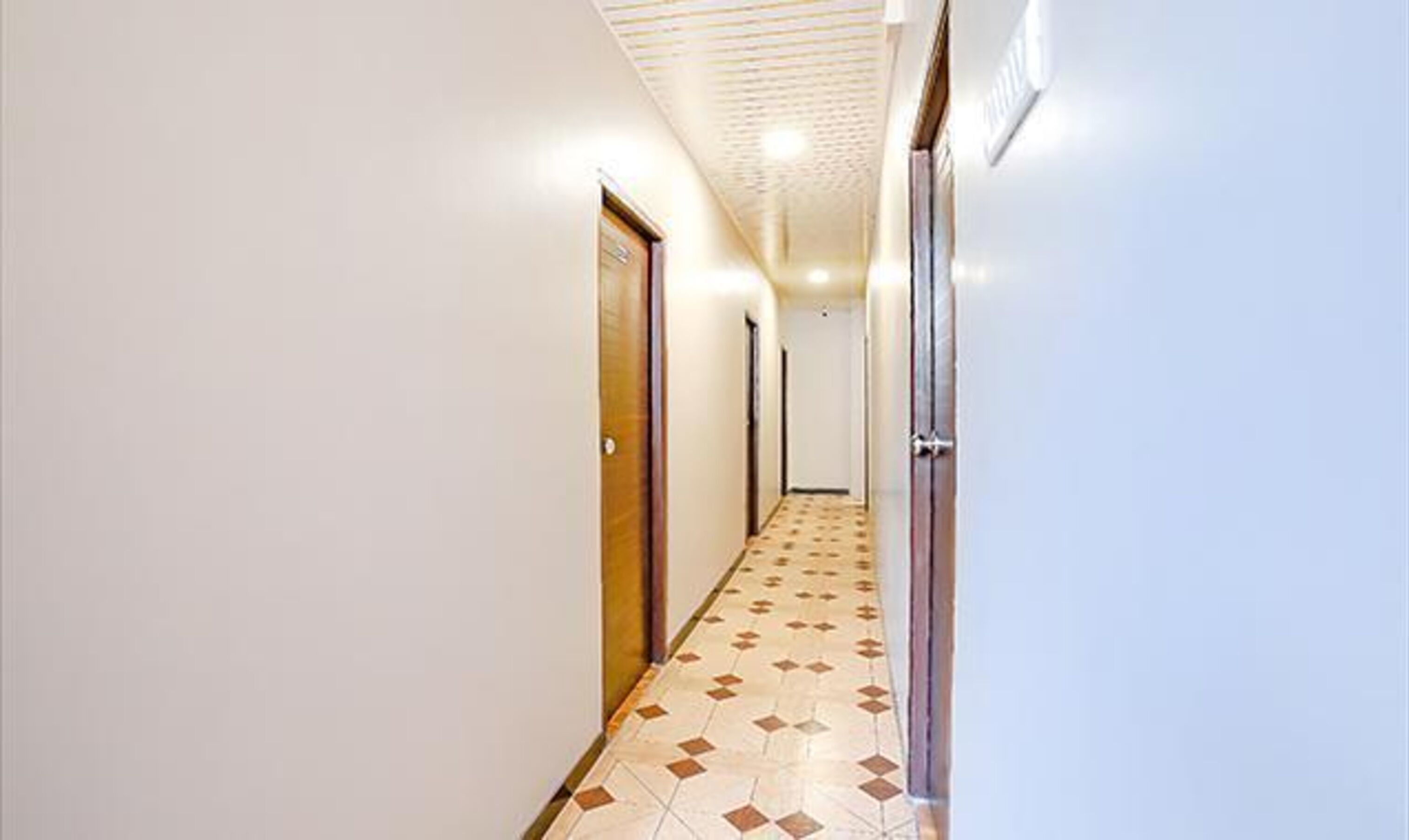 A hallway with patterned floor tiles, white walls, and doors on both sides.