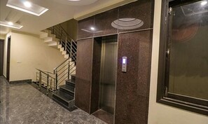 A modern elevator with a marble wall, a staircase with metal railings, and a ceiling with recessed lighting. - Fabhotel Agk (Haridwar)