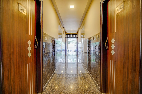 A polished hallway with wooden doors labeled G05 and G02, leading to a bright interior space. - Fabhotel Greenwood Xpress Inn (Bengaluru)