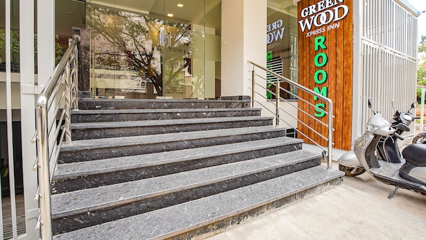 Un escalier en marbre mène à l’entrée d’un hôtel dont la façade est en verre et qui porte l’enseigne « Green Wood Xpress Inn ».