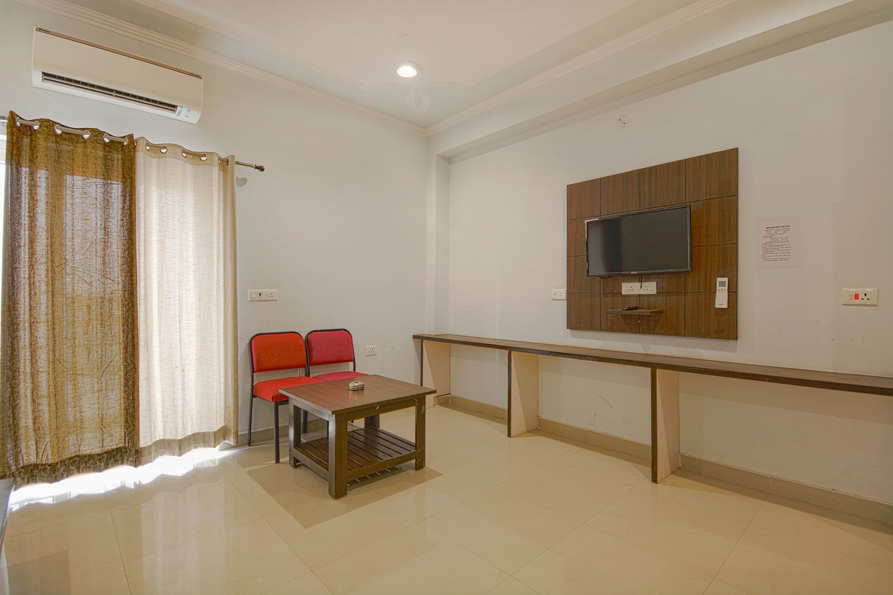 A room with a TV mounted on the wall, a table with chairs, and an air conditioning unit.
