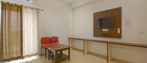 A room with a TV mounted on the wall, a table with chairs, and an air conditioning unit.