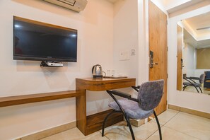 A hotel room with a wooden desk, a chair, a flat-screen TV, a coffee maker, and a mirror reflecting the room. - Fabhotel Blue Marine (Indore)
