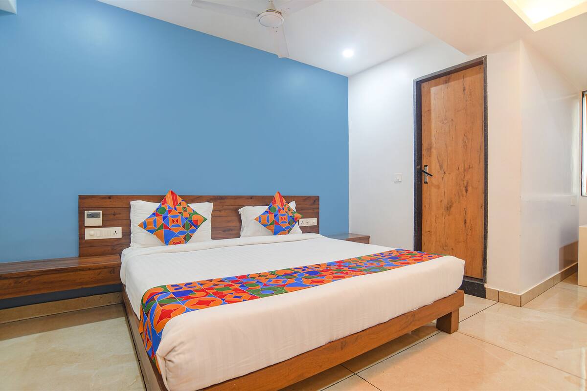 Quarto com cabeceira de madeira, cama com colcha colorida e parede azul.