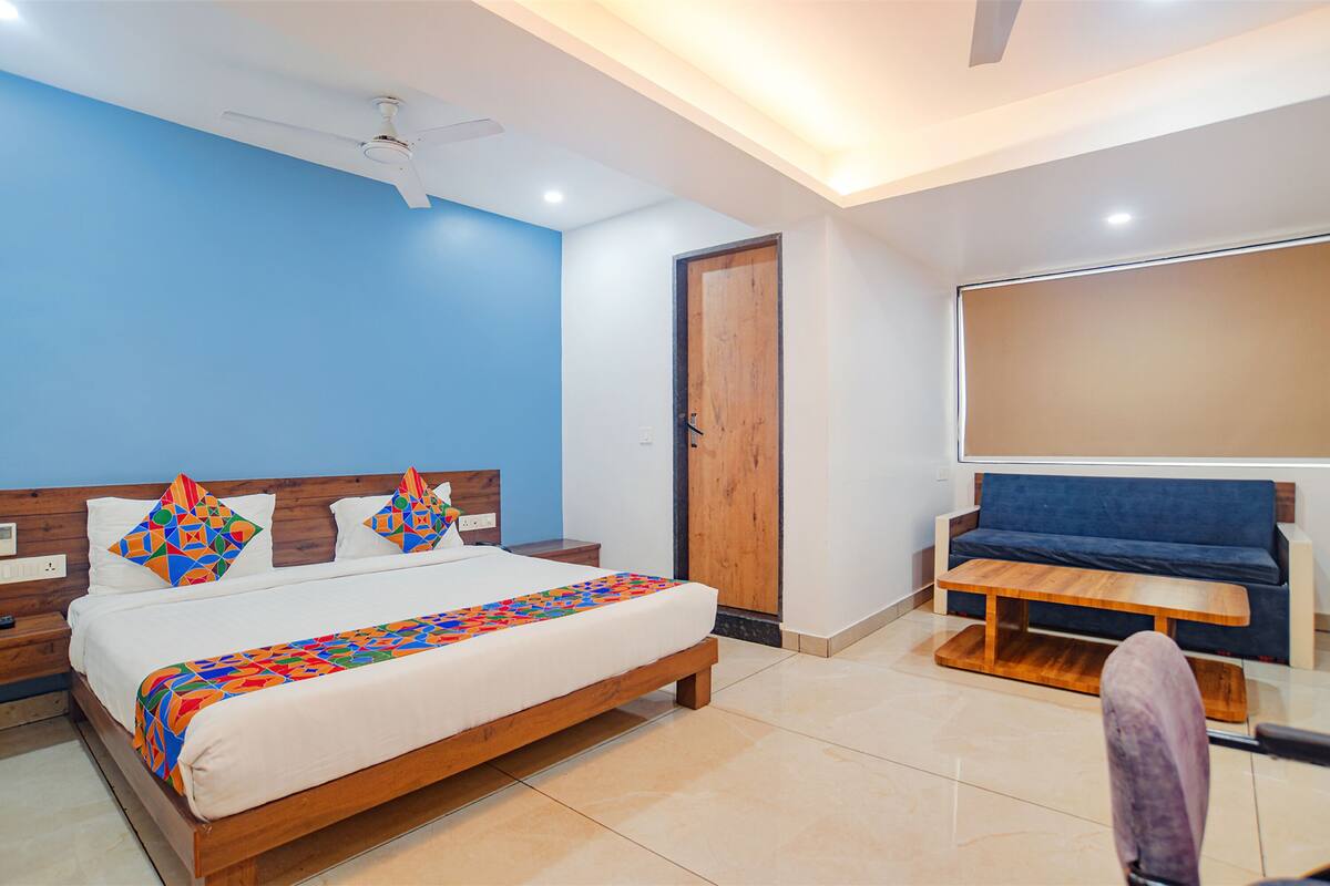 Quarto moderno com cama de madeira, parede azul, ventoinha no teto e um banco de madeira.