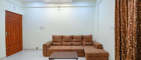 Una sala de estar con un sofá seccional, una mesa de centro de madera, una puerta de madera y una cortina.