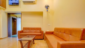 A living room with a sofa, a coffee table, and a wall-mounted fan. - Fabexpress Colaba Grand (Mumbai)