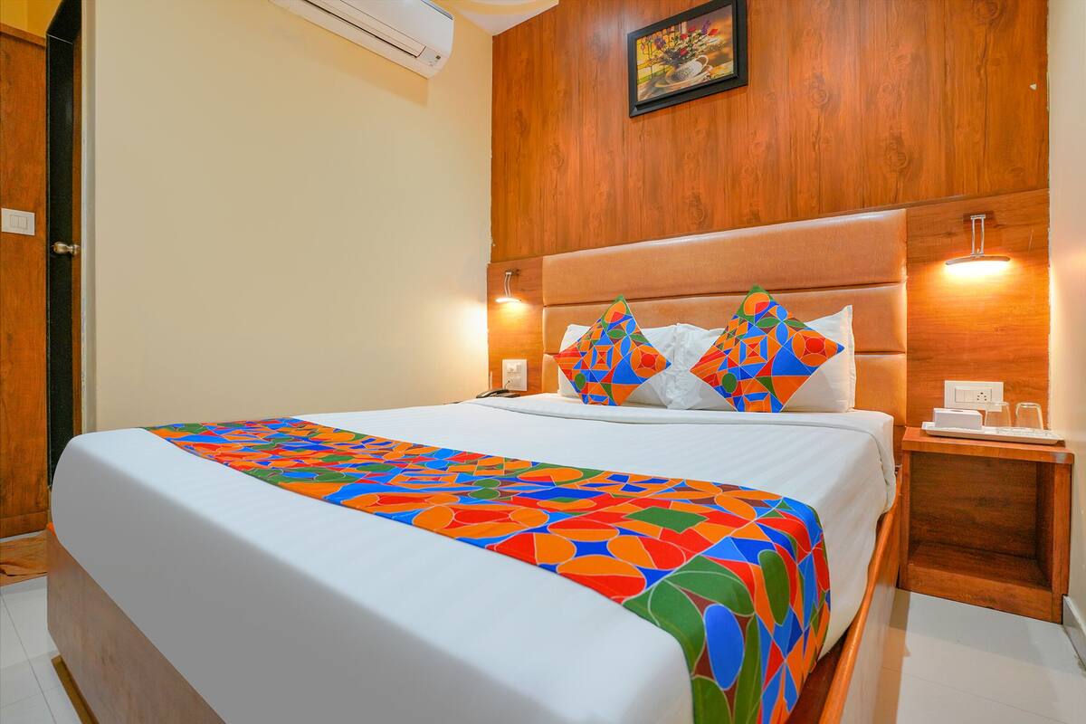 A hotel room with a large bed, wooden headboard, and a nightstand with a lamp.