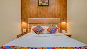 A hotel room with a wooden headboard, two bedside lamps, a telephone, and a colorful geometric-patterned bedspread. - Fabexpress Colaba Grand (Mumbai)