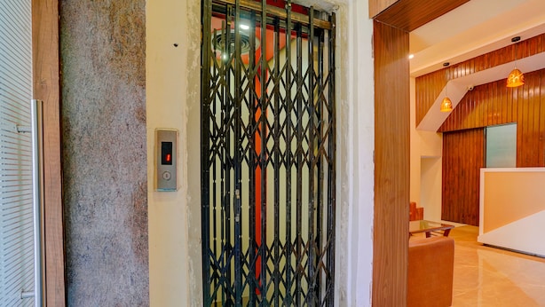 A modern reception area with a wooden reception desk, a glass partition, and a digital elevator control panel. - Fabexpress Colaba Grand (Mumbai)