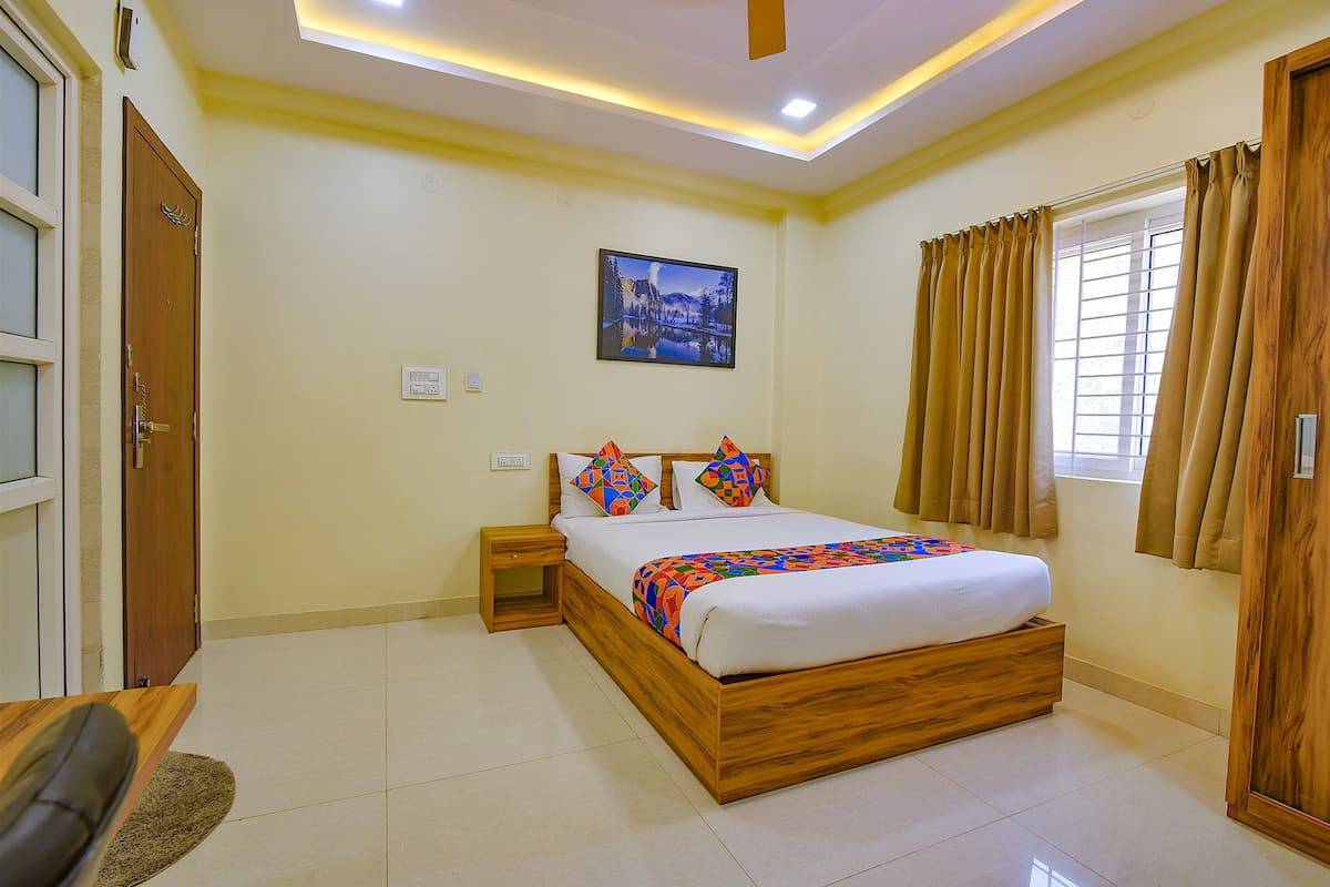 Quarto com cama de madeira, mesa de cabeceira, TV na parede e janela com cortinas.