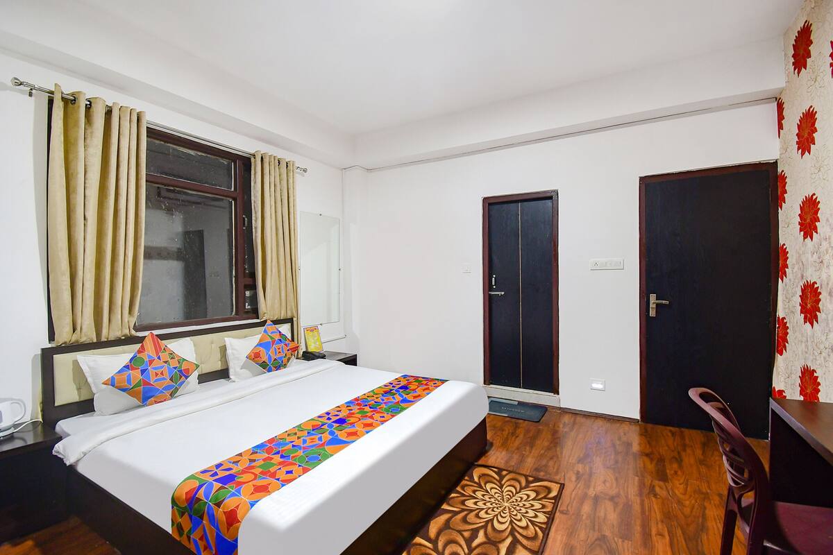 A hotel room with a bed, a wooden floor, a desk, and a chair.