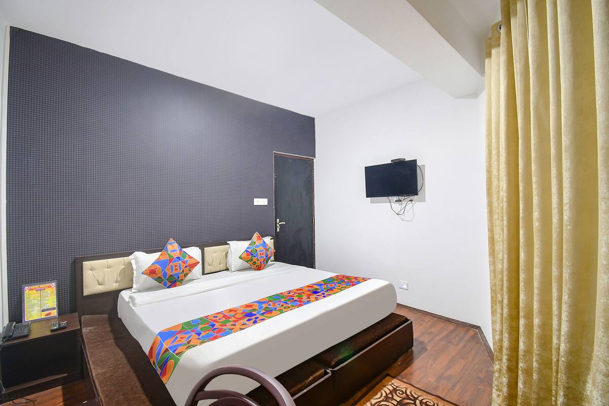 A hotel room with a large bed, a flat-screen TV mounted on the wall, and a wooden floor.