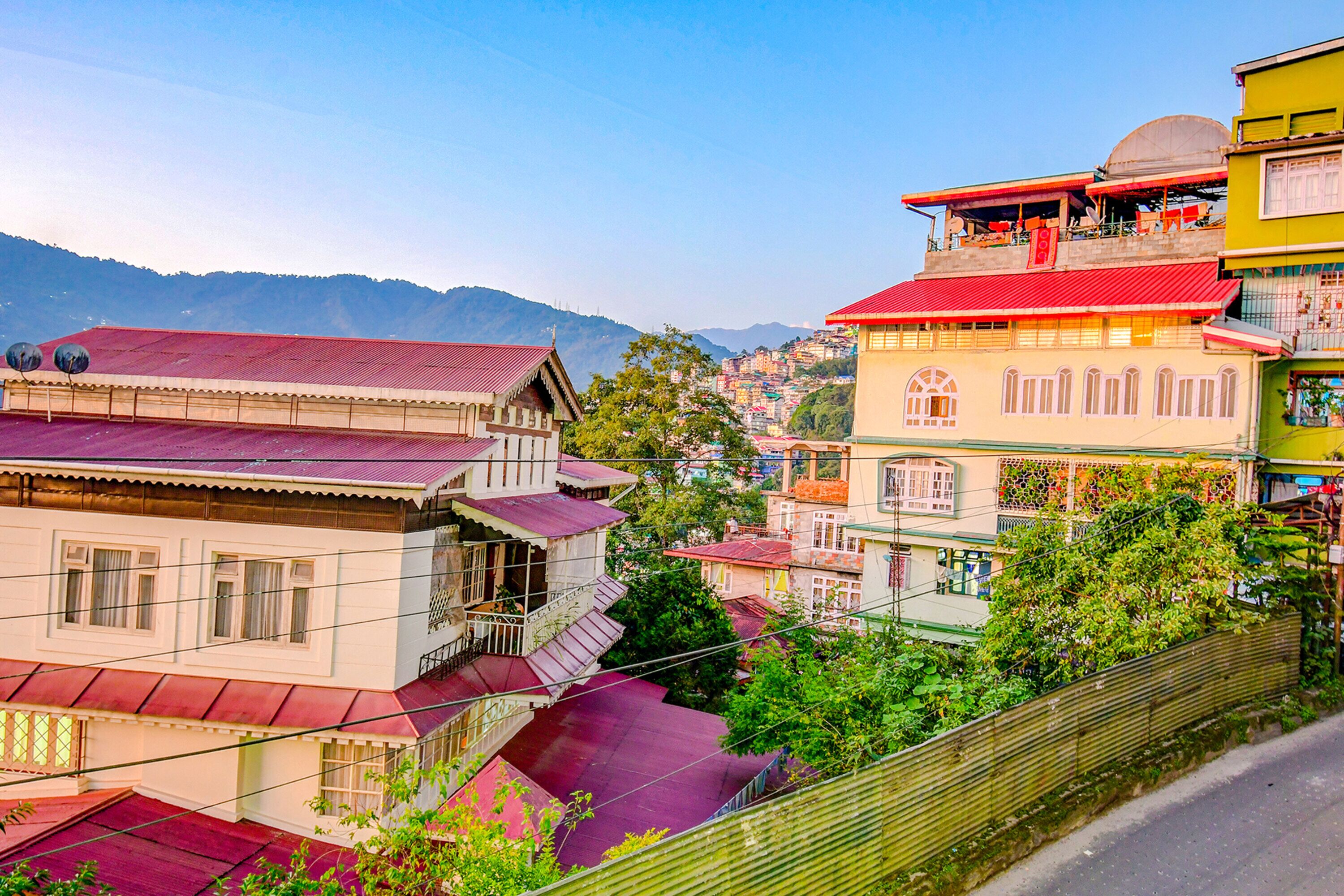 A multi-story building with balconies, a red roof, and a view of a mountainous landscape.