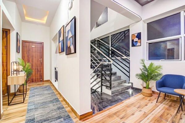 A modern interior with a wooden floor, a blue sofa, a staircase, and abstract art on the walls. - Via Rithun Residency - jayanagar (Bengaluru)