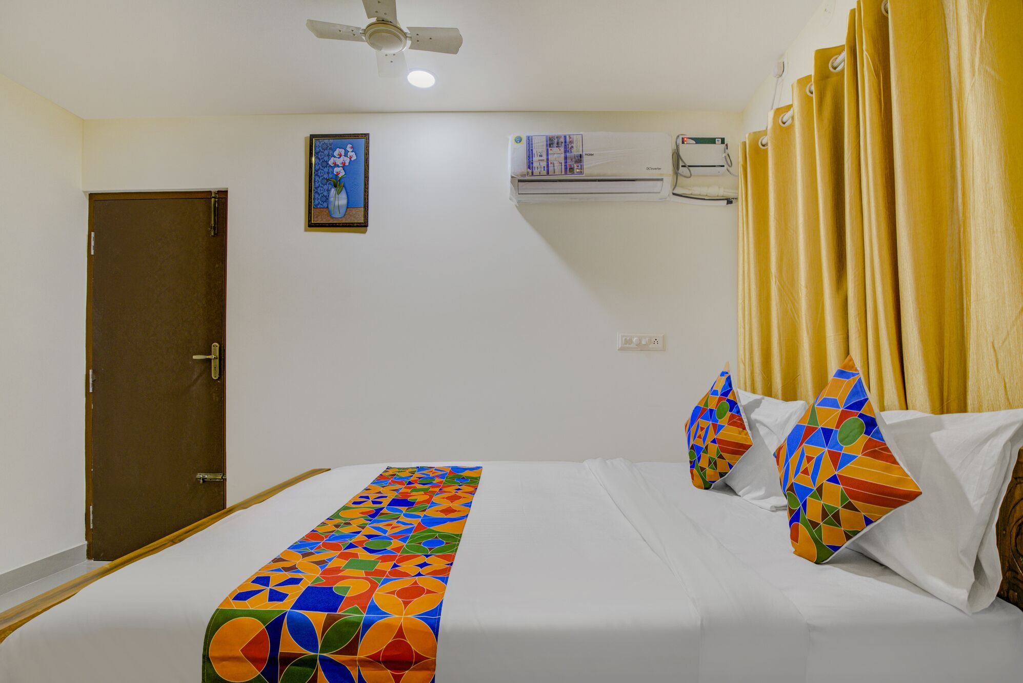 A hotel room with a bed, a ceiling fan, an air conditioning unit, and a door.