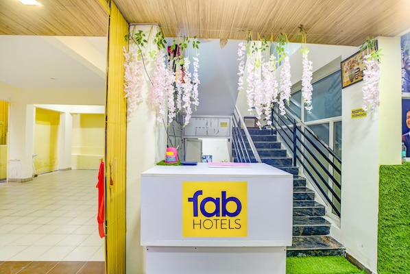Een receptiebalie met een bordje voor Fab Hotels, een trap en bloemversiering.