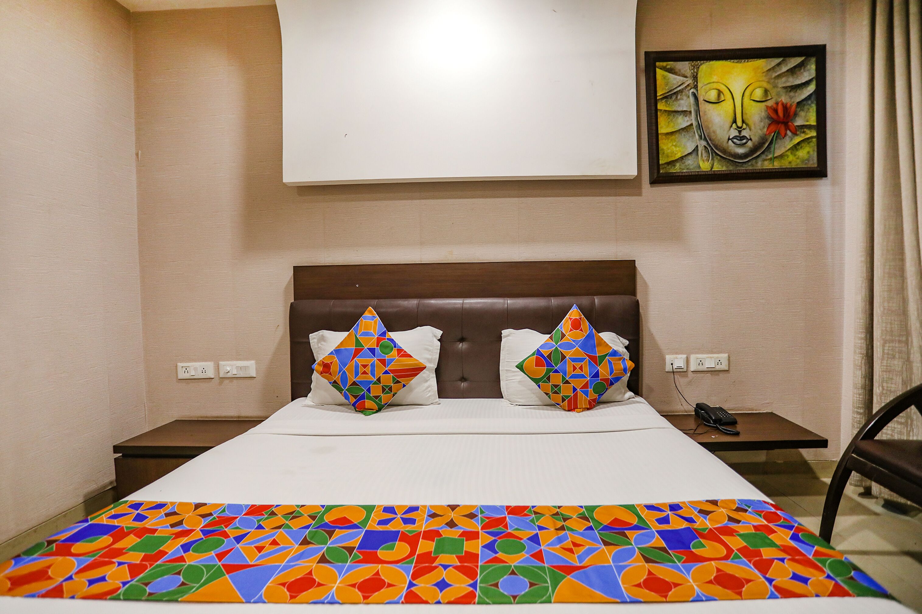A hotel room with a bed, two pillows, a bedside table, a phone, and a wall-mounted painting.