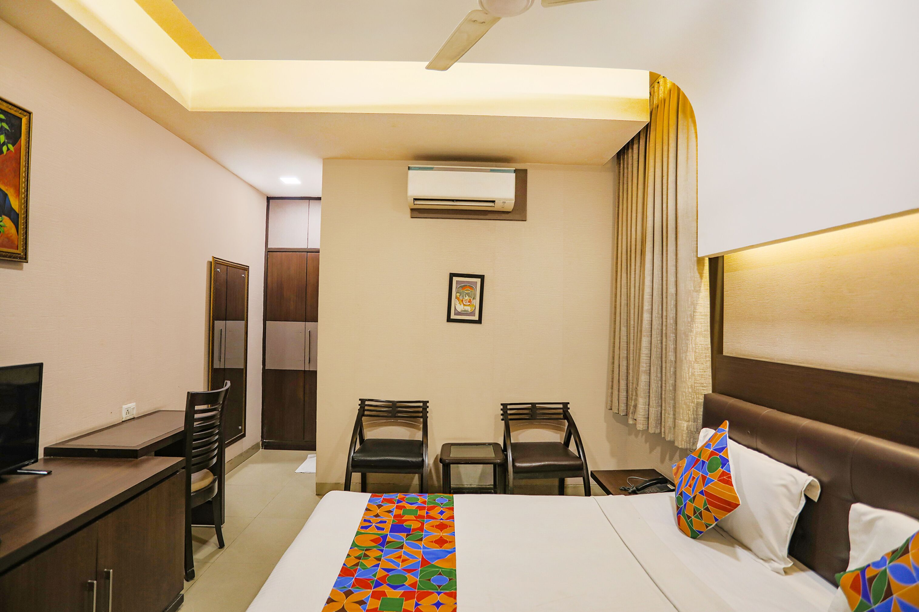 A hotel room with a bed, desk, chairs, and an air conditioning unit.