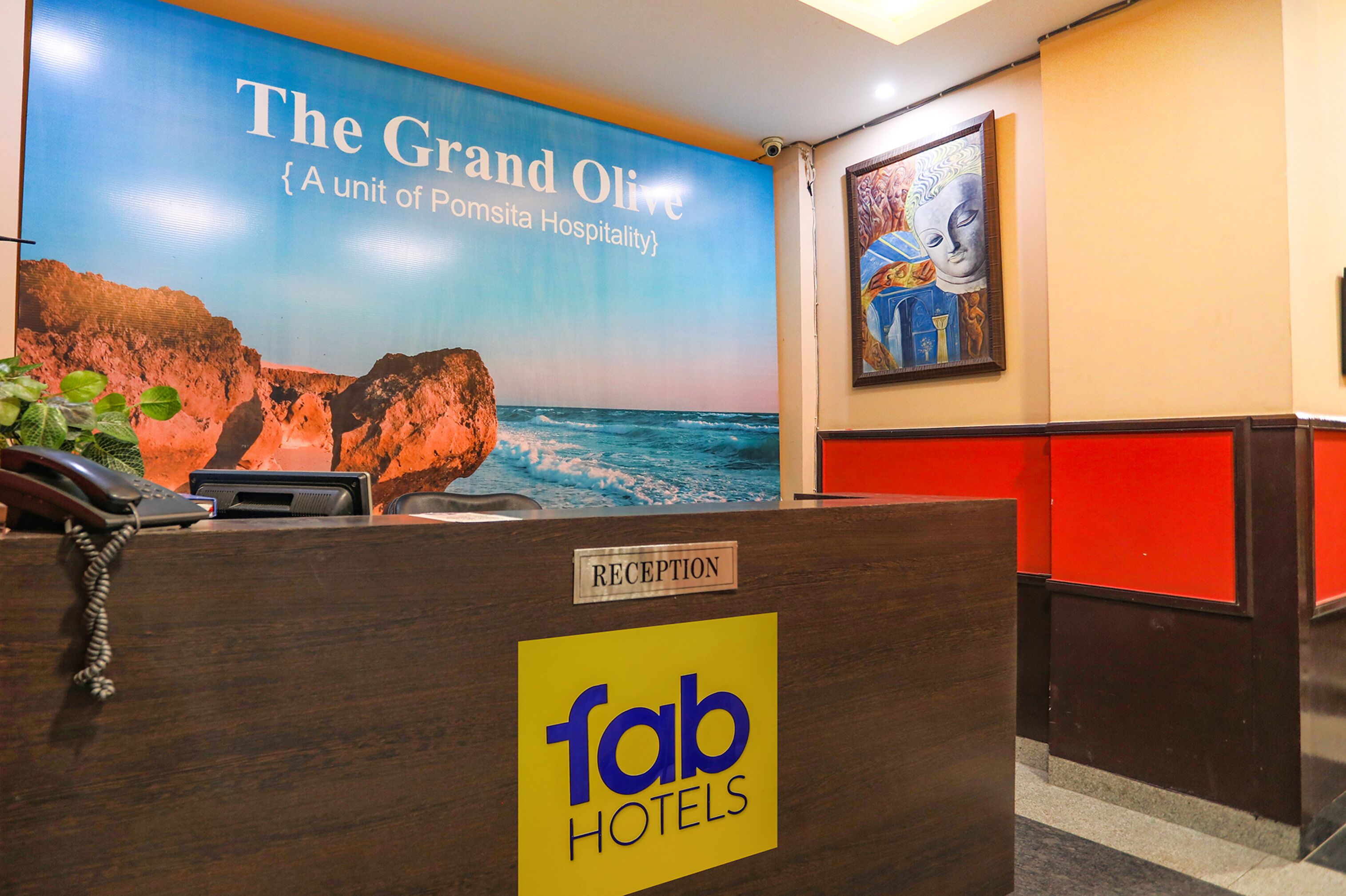 A reception desk with a sign for 'fab hotels' and a backdrop featuring 'The Grand Olive' with a coastal scene.