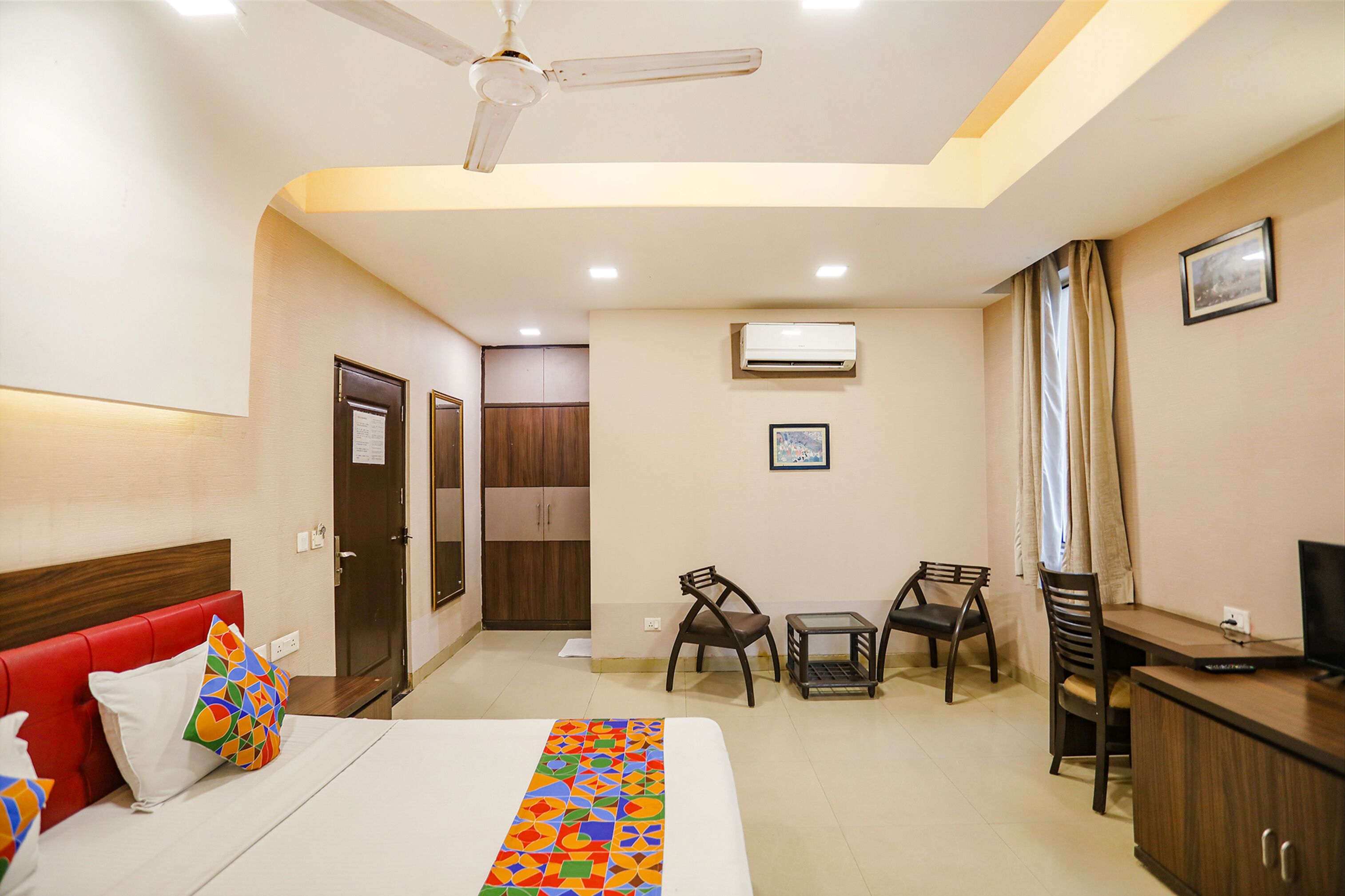 A hotel room with a bed, a desk, a chair, a television, and a ceiling fan.
