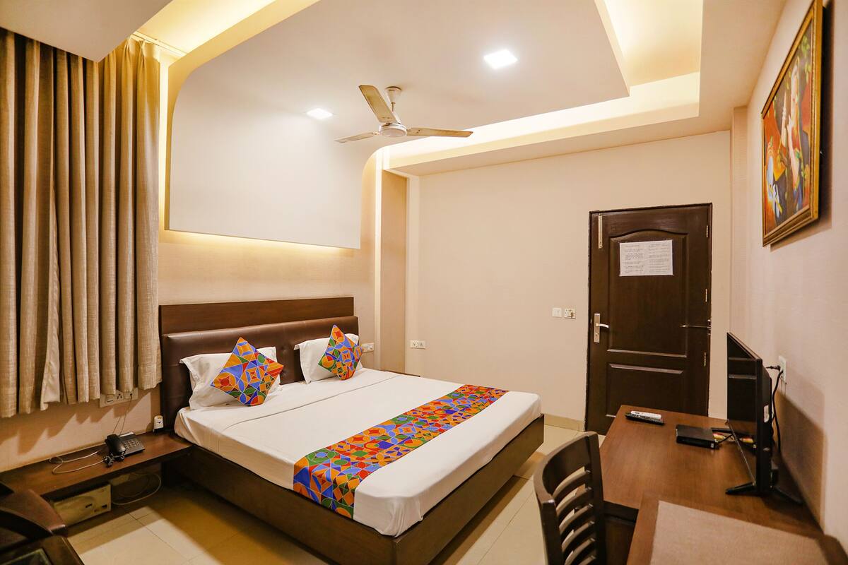 A hotel room with a bed, bedside table, desk, chair, ceiling fan, and a door.