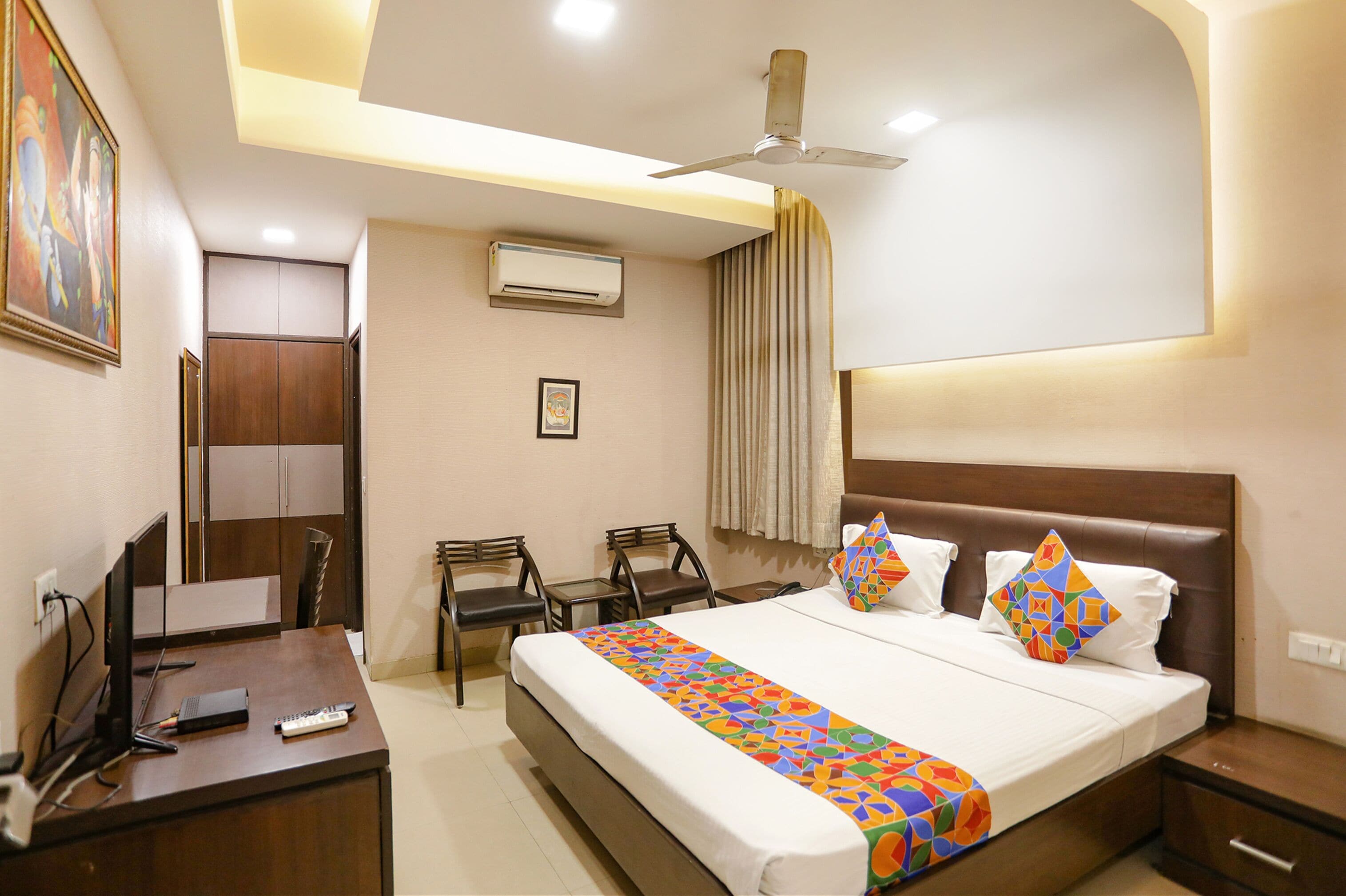 A hotel room with a bed, desk, chairs, and a ceiling fan.