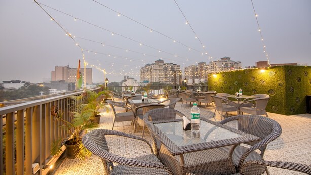 An outdoor seating area with wicker tables and chairs, string lights, and a view of city buildings. - Itsy Hotels NV, Sushant Lok (Gurugram)