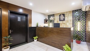 A reception area with a wooden reception desk, a black door, and potted plants. - Itsy Hotels NV, Sushant Lok (Gurugram)