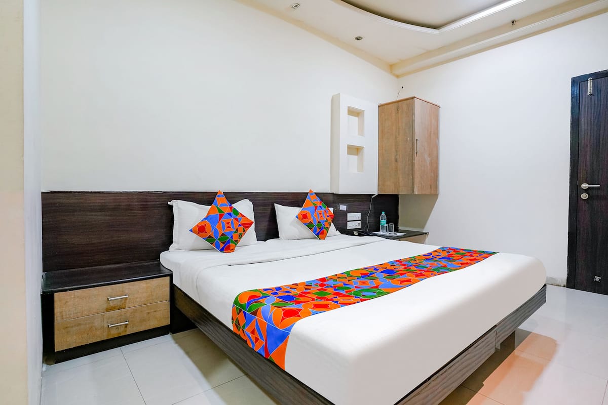 Una cama bien hecha con una manta colorida, un cabecero de madera y una mesita de noche con una lámpara.