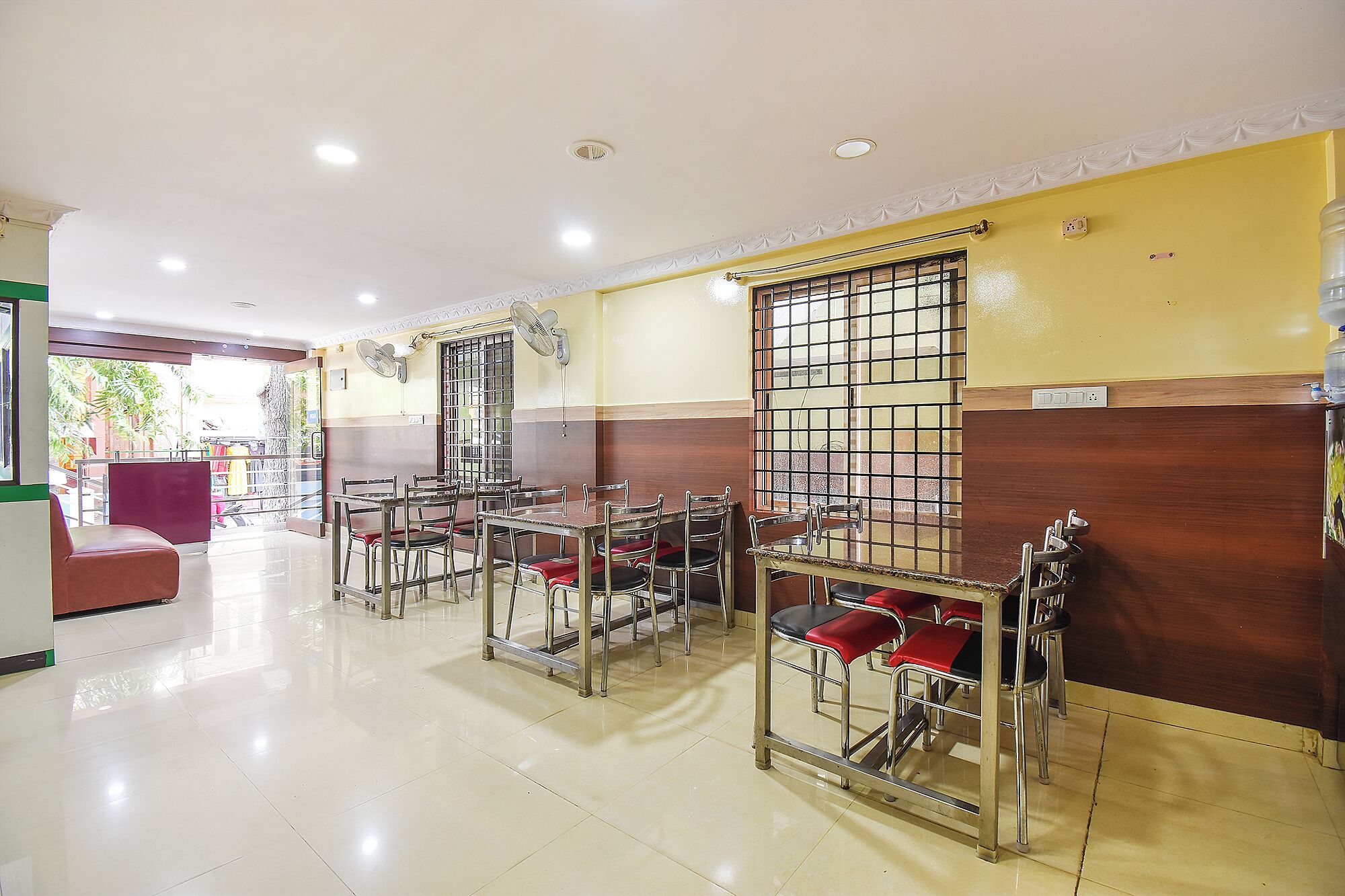 A dining area with tables and chairs, a window with bars, and ceiling fans.