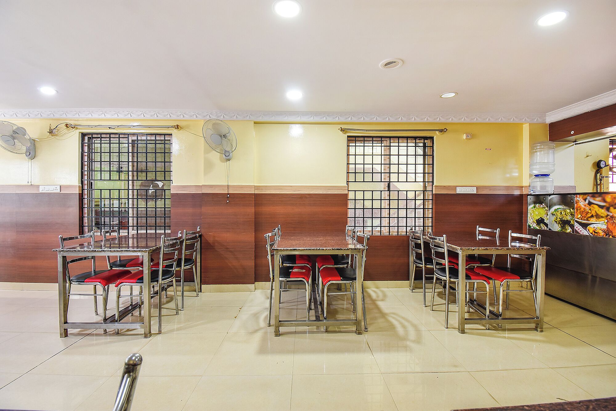 A dining area with tables and chairs, a tiled floor, and a kitchen area with food display.