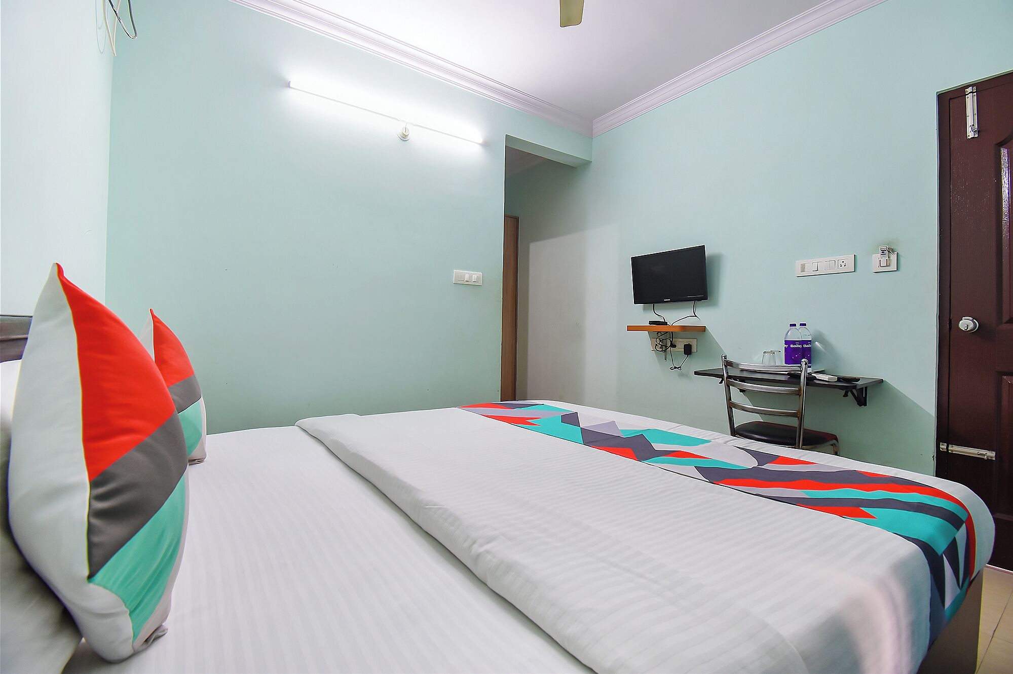 Habitación de hotel con cama, escritorio, silla, televisor y puerta.