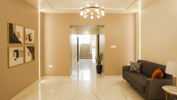 A spacious hallway with a marble floor, a staircase, a grey sofa with an orange pillow, and a chandelier. - Fabhotel Happy Homely Stay (Pune)