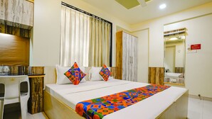 A hotel room with a bed, a desk, a chair, a wardrobe, and a mirror. - Fabhotel Happy Homely Stay (Pune)