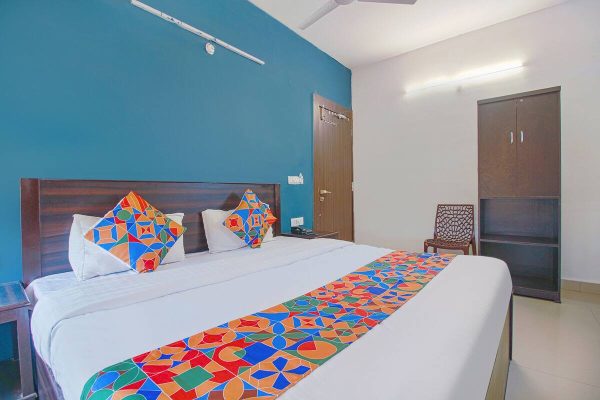 A hotel room with a large bed, a wooden headboard, a blue accent wall, a wardrobe, and a chair.