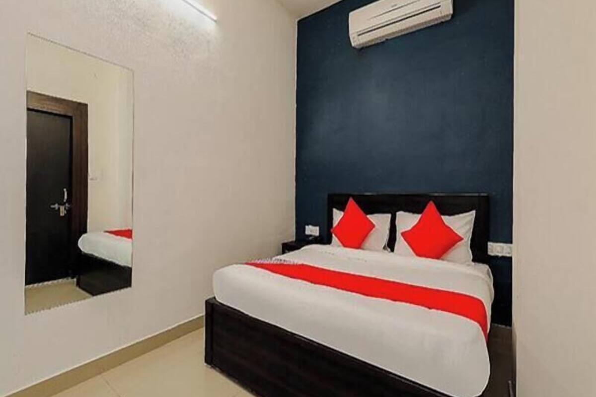A hotel room with a bed, a mirror, and an air conditioning unit.