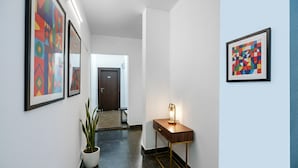 A hallway with a potted plant, a wooden side table with a lamp, and two framed abstract artworks on the walls. - FabHotel Saket Inn (Bhopal)
